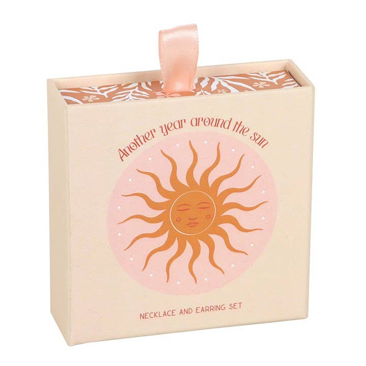 Necklace and earring set packaging with sun design and text on a white background