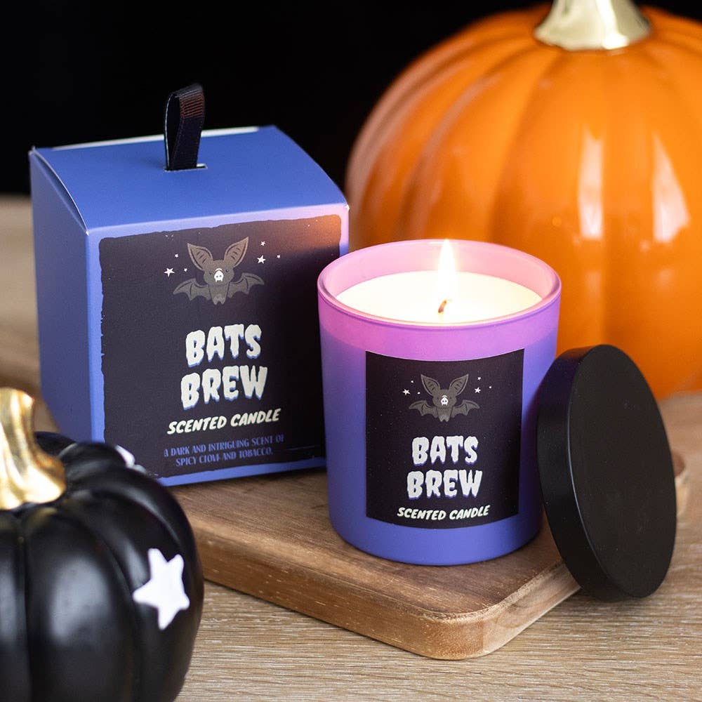 Scented candle labeled 'Bats Brew' with packaging and pumpkins on a wooden surface