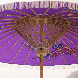 Purple parasol with decorative patterns and white fringe on a white background
