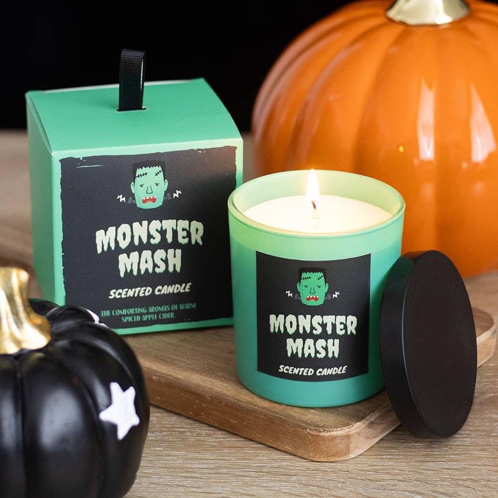 Monster Mash scented candle with packaging and pumpkins on a wooden surface