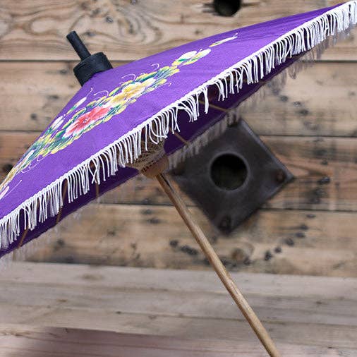 Purple outdoor umbrella with floral design and white fringe on a wooden surface