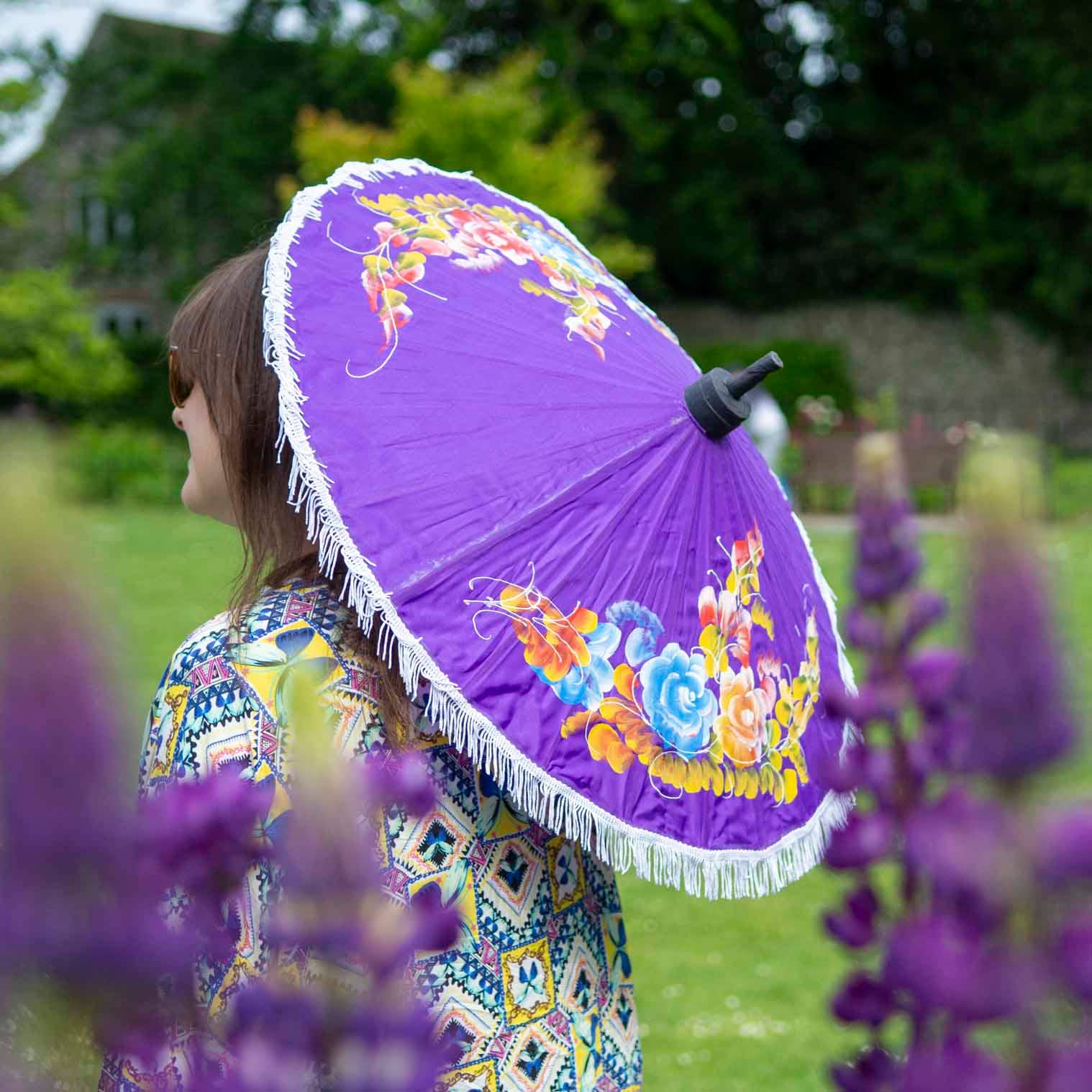 Person holding a purple floral umbrella in a garden setting