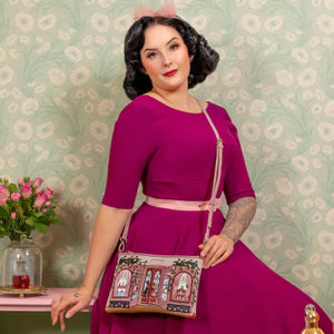 Woman in a vintage-style dress holding a decorative handbag against a floral wallpaper background