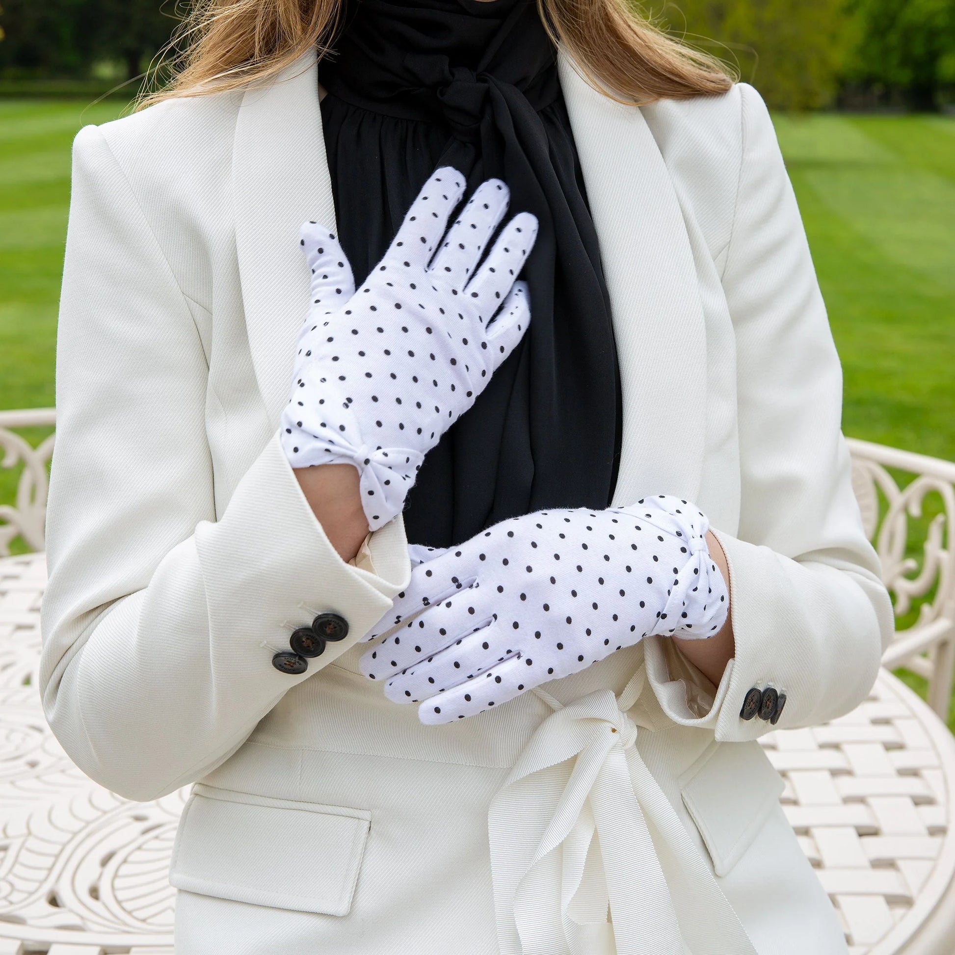 Person wearing white polka dot gloves with a blurred green outdoor background